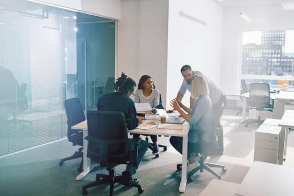 Focused group of diverse work colleagues having a meeting together around a table inside of a glass walled office