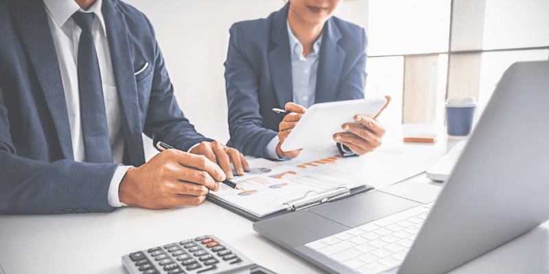 two business people at a table with their pens, paper, and laptop