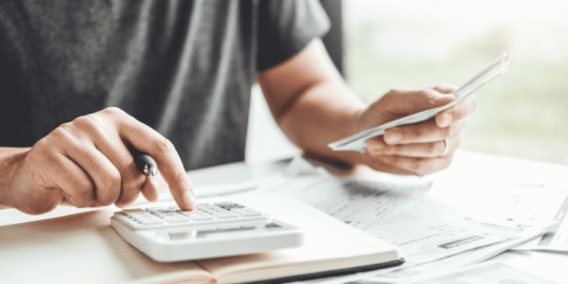 A zoomed in view of a man using a calculator and taking financial notes.