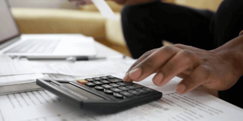 fingers on a calculator with papers on a table.