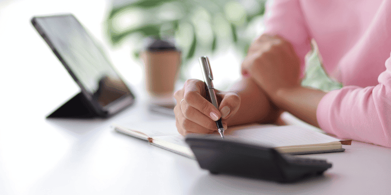 woman in pink writing at a desk with an open check book
